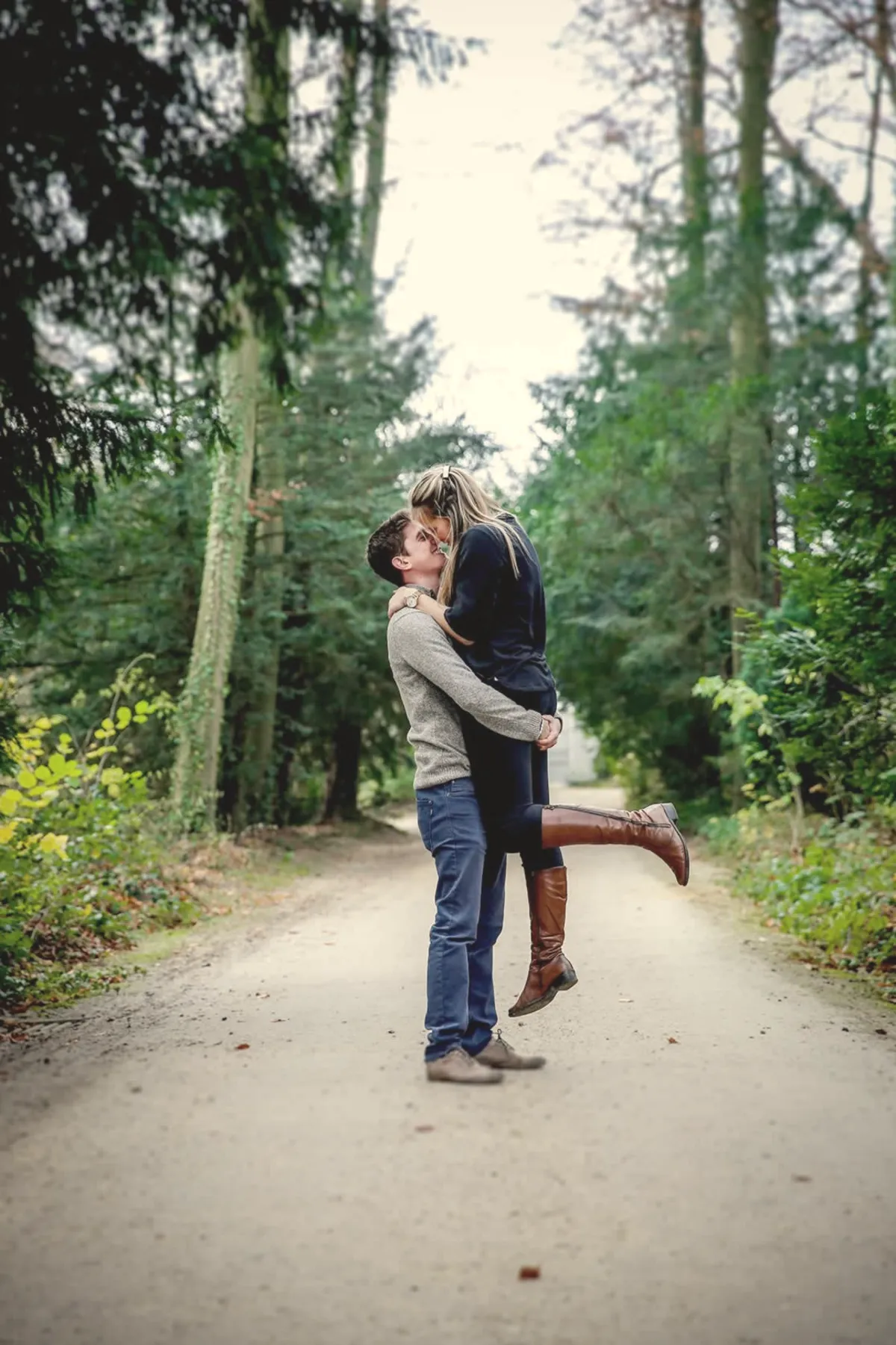 Séance engagement : le couple s’embrasse sur un chemin forestier.
